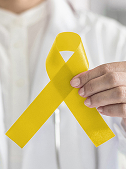 A person in a white lab coat with a stethoscope around their neck holds up a gold ribbon.