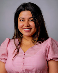 A woman with long brown hair wearing a pink blouse smiles at the camera.
