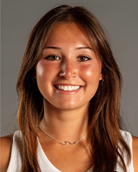 A woman with long brown hair wearing a white tank shirt smiles at the camera.