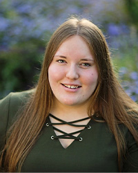 A woman with long brown hair wearing a green shirt smiles at the camera.