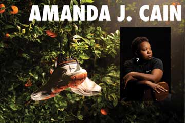 The name Amanda J. Cain is bold across the top of the image. There is an orange tree with a pair of Nike Air Jordans hanging in it. There is also a headshot of Amanda, sitting in a chair, wearing all black with a black background.