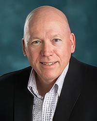 Headshot of Roger Hart on a soft turquoise backdrop.