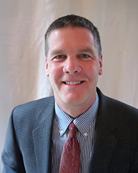 Headshot of John McDonald in front of a white plaster wall.