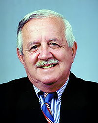 Headshot of David C Smith in a suit and tie in front of a blue backdrop