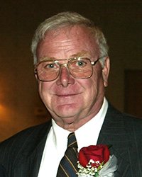 Headshot of Neal R Miller in a suit and tie with a red rose boutonnière