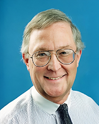 Headshot of Ralph Langer, in a shirt and tie in front of a blue backdrop