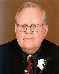 Headshot of William George Serrin, Jr. wearing a suit and tie in front of a dark gold backdrop