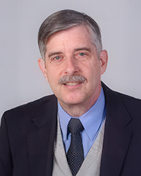 Headshot of Paul Chaffee in a jacket and tie, in front of a soft grey backdrop
