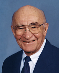 Headshot of Richard Milliman in a suit and tie, in front of a deep blue backdrop