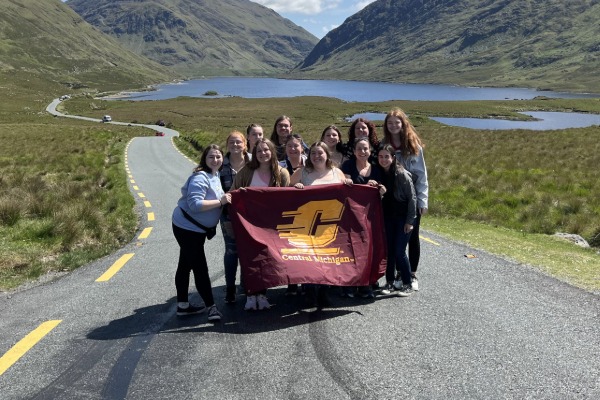A group of students posing for a photo on a road in Ireland, holding a big CMU flag.
