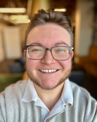 2026-04-10-Bryce-Thomas-01-200x250 A headshot of Bryce Thomas wearing a grey polo and glasses.