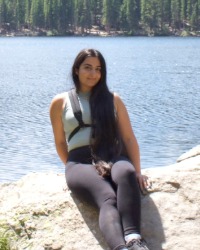 2026-04-10-Emily-Awad-01-200x250 Emily Awad sitting on a rock in front of a lake.