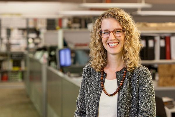 a woman with shoulder length, curly, blond hair and glasses smiling at the camera