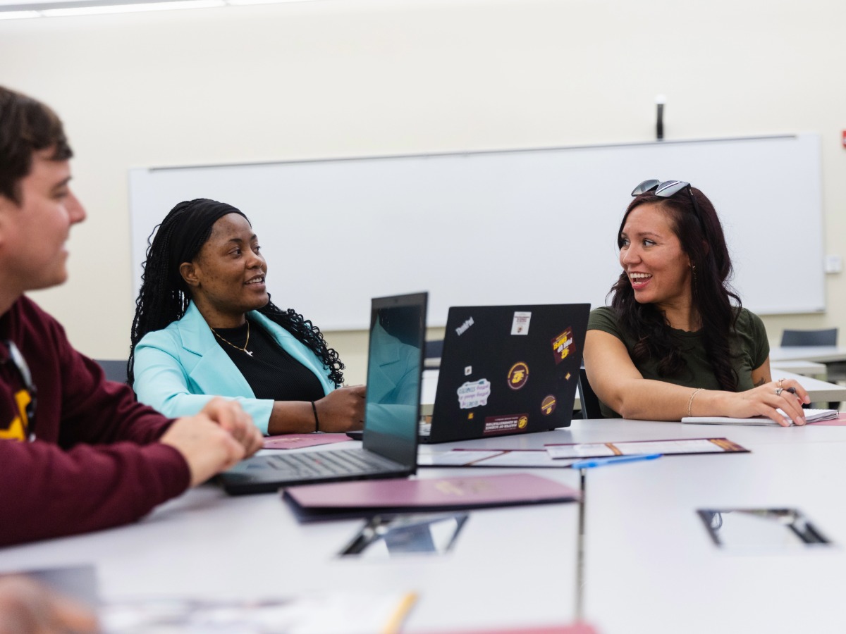 A group of students sitting smiling and talking with each other while sitting at a table in a classroom.