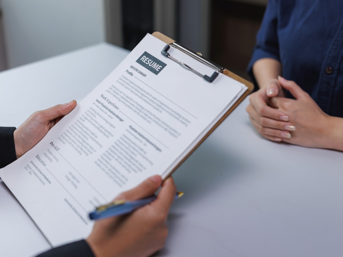 A person holding a resume on a clipboard with a pen.