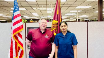 Saraswathi Nemani and Dr. Jon Hummiston pose in an Online and Innovation office with an American flag and a maroon CMU flag in the background.