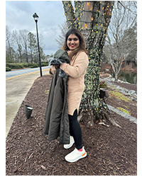 Yamini Iyer- MSA Peer Mentor, standing outside in front of a tree while holding a jacket, smiling for a photo.