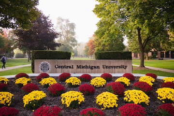 A Central Michigan University stone sign with the seal behind a maroon and gold garden.