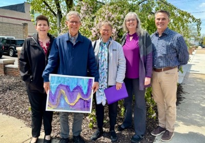 A group of people standing outside with one person holding up a blue and purple painting.