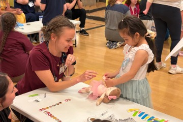 A PA student sitting at a table and talking with a child holding a stuffed animal.