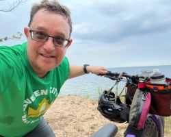Joe Lubig posting with his bike with sand and a lake behind him.