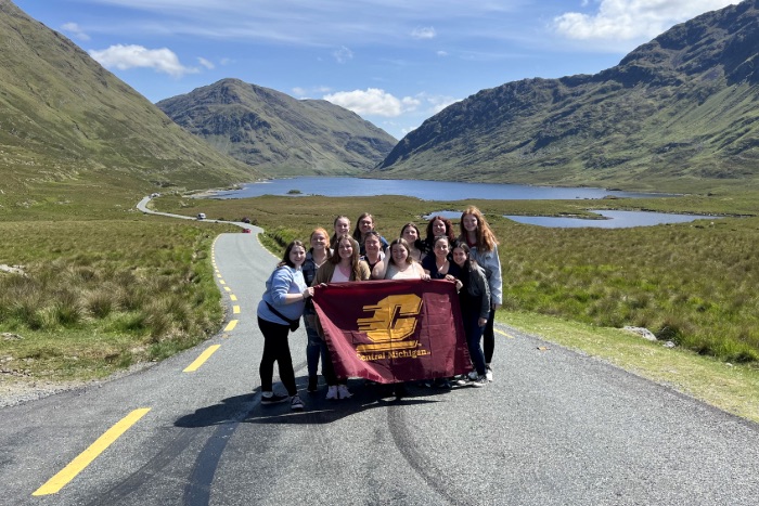 20251119-Ireland-Study-Abroad-2024-01-700x467 Students posing in front of mountains in Ireland with the CMU flag.