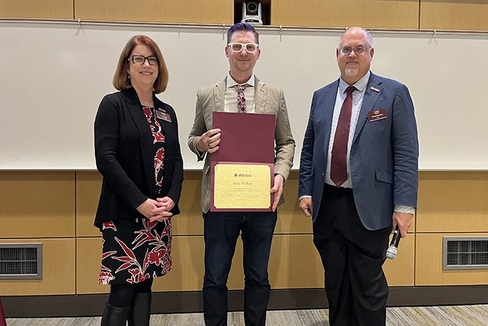 Alumni award recipient Kris Phillips holds a certificate and stands between Associate Dean Marcy Taylor and Dean Richard Rothaus.