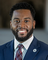 Closeup image of LaMarcus D. Howard wearing a navy blue suit and maroon plaid tie.