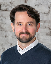 Closeup image of Dan Nikolits wearing a dark sweater with a white collar.