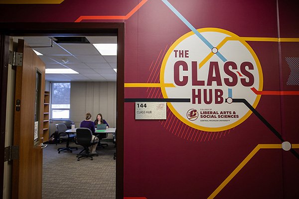 Doorway into the CLASS HUB showing logo on wall and two individuals are seated at table inside the room