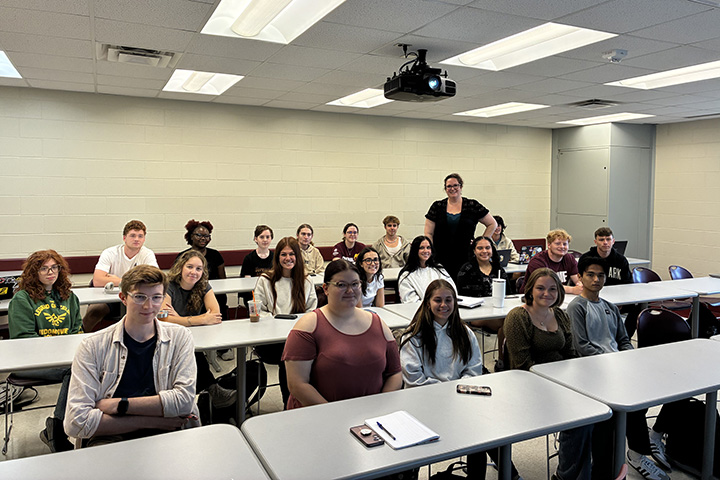 Nicole Sparling Barco wearing black stands in the middle of rows of her students seated at tables in her classroom.