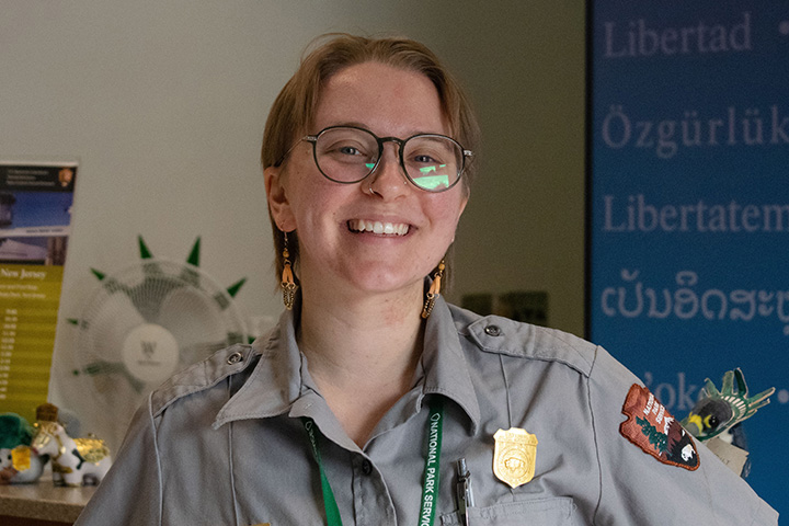 Fern Borus wearing a National Park Service uniform while standing at the information desk for the Statue of Liberty National Monument.