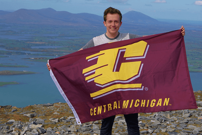 Student on mountain top holding CMU flag