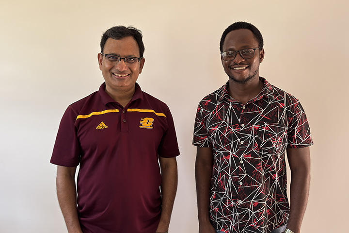 Prakash Adhikari  wearing a maroon Central Michigan University shirt stands next to Ernest Pondani wearing a red and white patterned shirt.