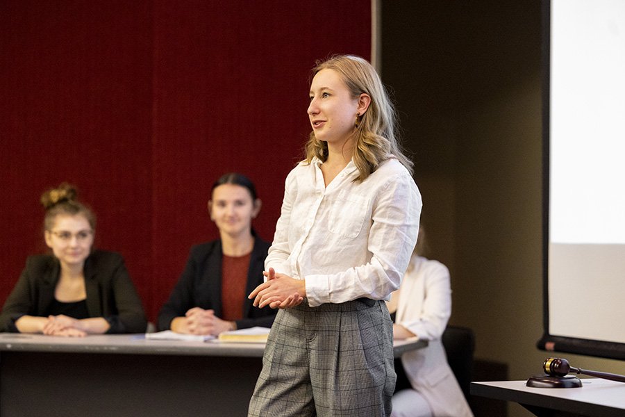 Student wearing a white shirt and grey pants speaks during a mock trial presentation.