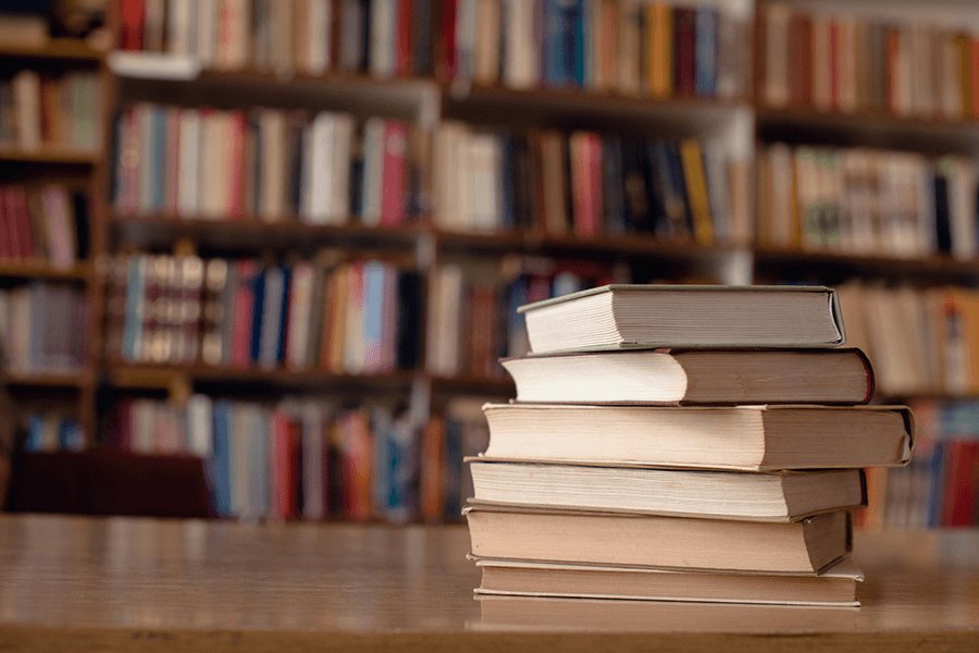 Stack of creative writing books on a table in front of full bookshelves.