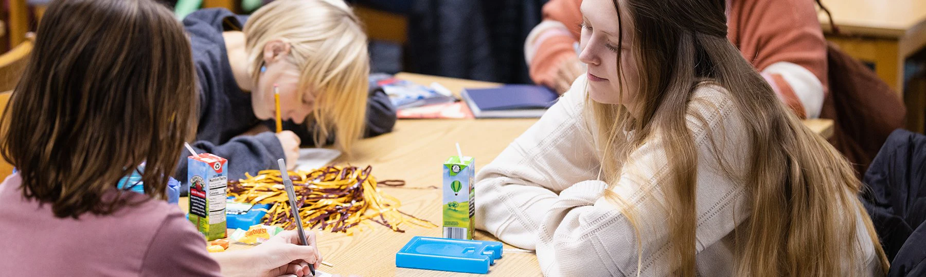 CMU student sits at table observing two younger students writing.