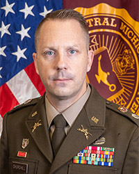 Closeup image of LTC Robert Churchill wearing a military uniform with numerous medals while in front of the American flag and CMU flag