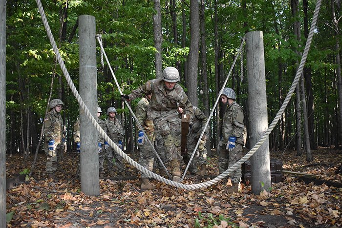 Military Science cadet wearing military uniform walks across ropes in the wooded Field Leaders Reaction Course.