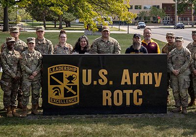 Department of Military Science and Leadership cadets and staff stand next to the U.S. Army ROTC sign on the campus of Central Michigan University.