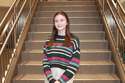 20260511_Alison A woman with brown hair wearing a striped shirt standing in front of a staircase.