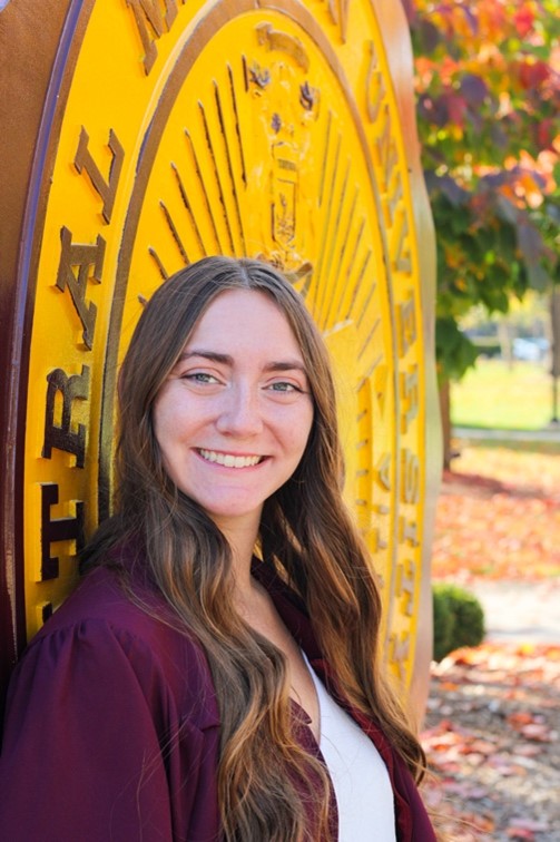 A woman with long brown hair standing in front of the CMU seal.