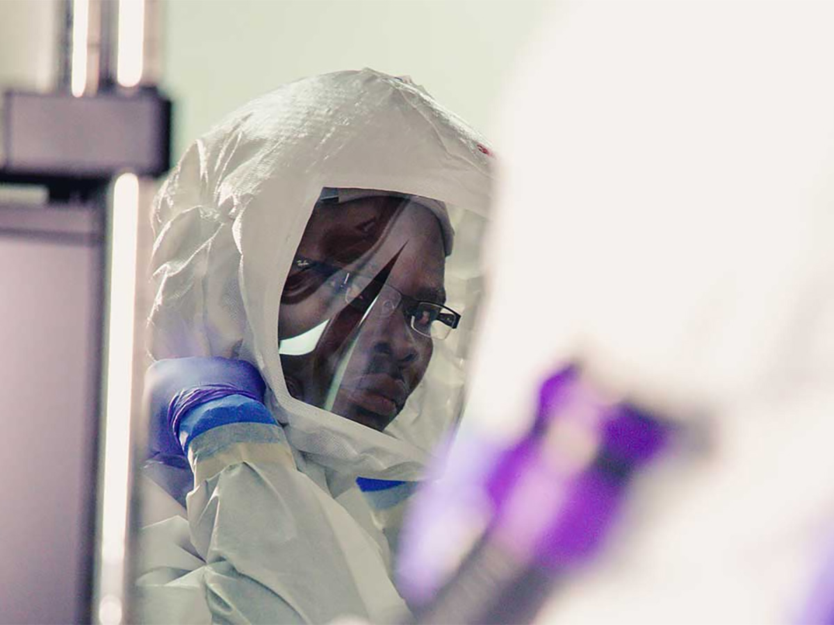 A man with glasses wearing a white haz-mat suit in a laboratory.