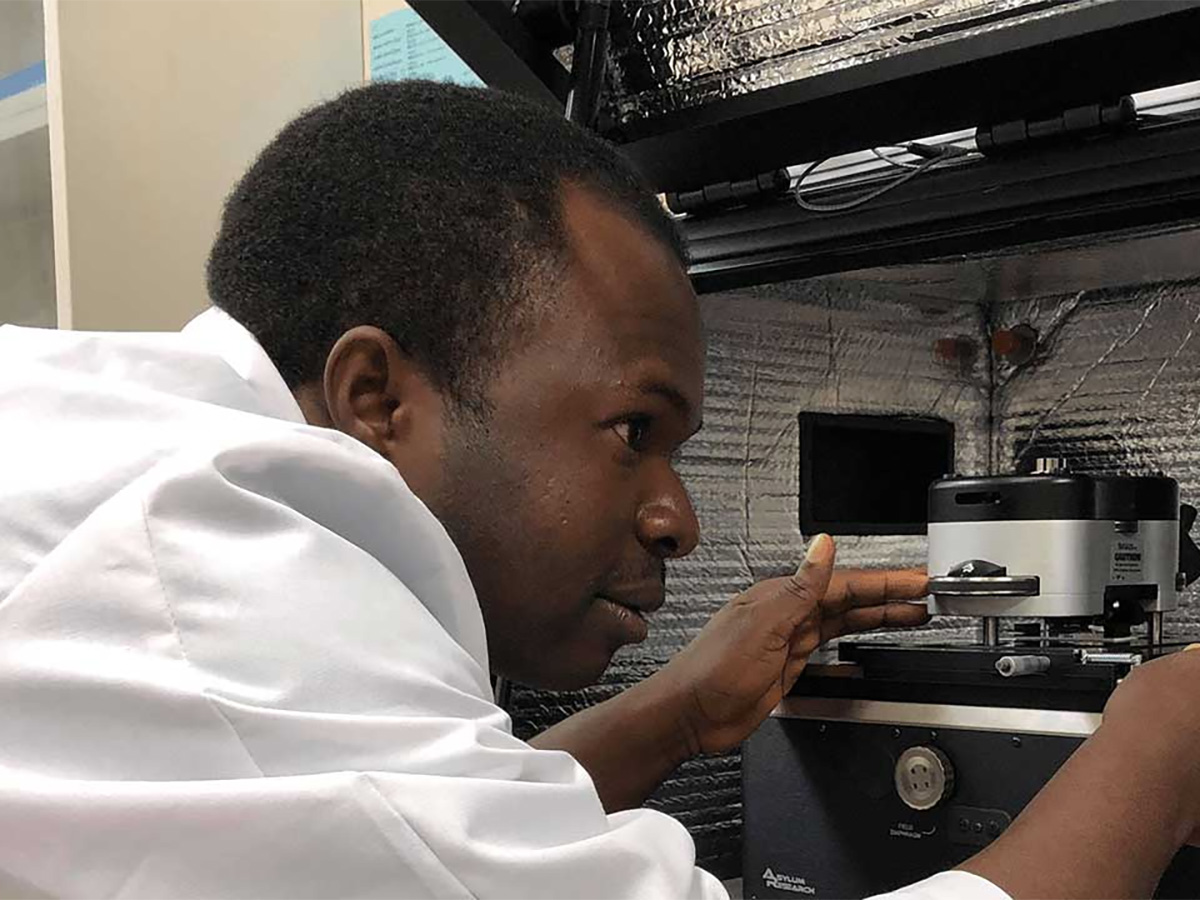 A man in a white lab coat examining a scientific device in a lab.