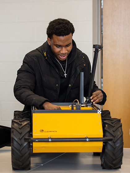 A Student working on a yellow four wheeled robot.