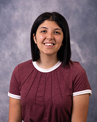 20250917_SydneeAllen_200x250 A woman in a maroon shirt and dark hair in front of a grey background.