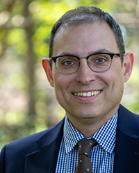 A man with dark hair wearing glasses and a suit.