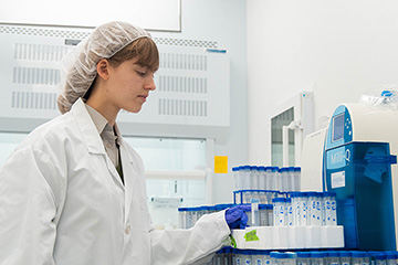 A  woman in a lab coat with vials around her in a chemistry lab.