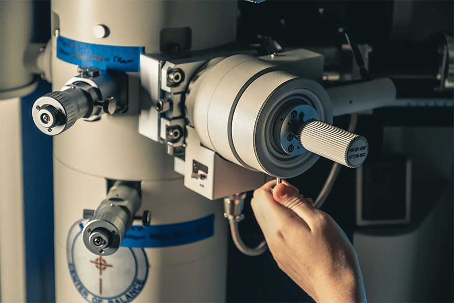 A hand reaches a knob on a microscope