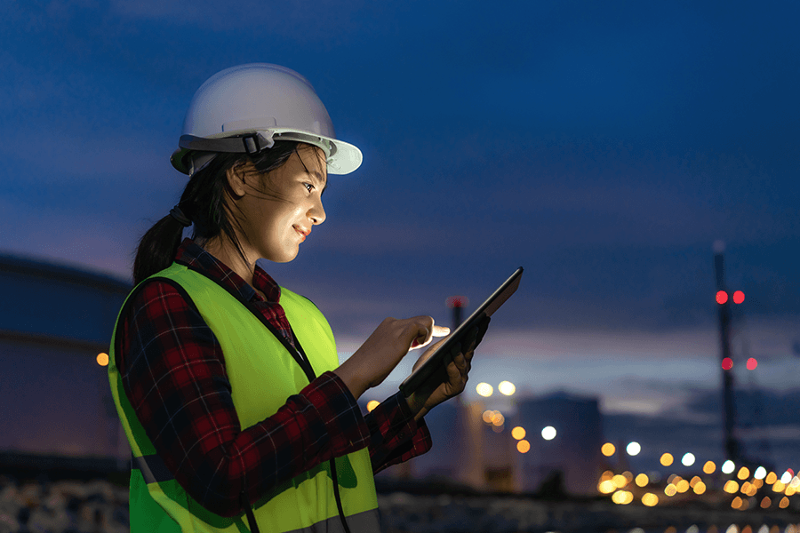 An engineer in a hard hat and vest checks a tablet screen.